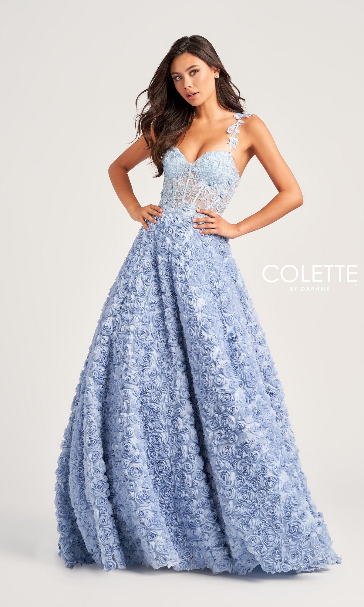 A woman models the Colette Light Blue Long Rosette Prom Gown CL5250, featuring 3-D rosettes, a fitted bodice, and a full floor-length a-line skirt against a plain background.